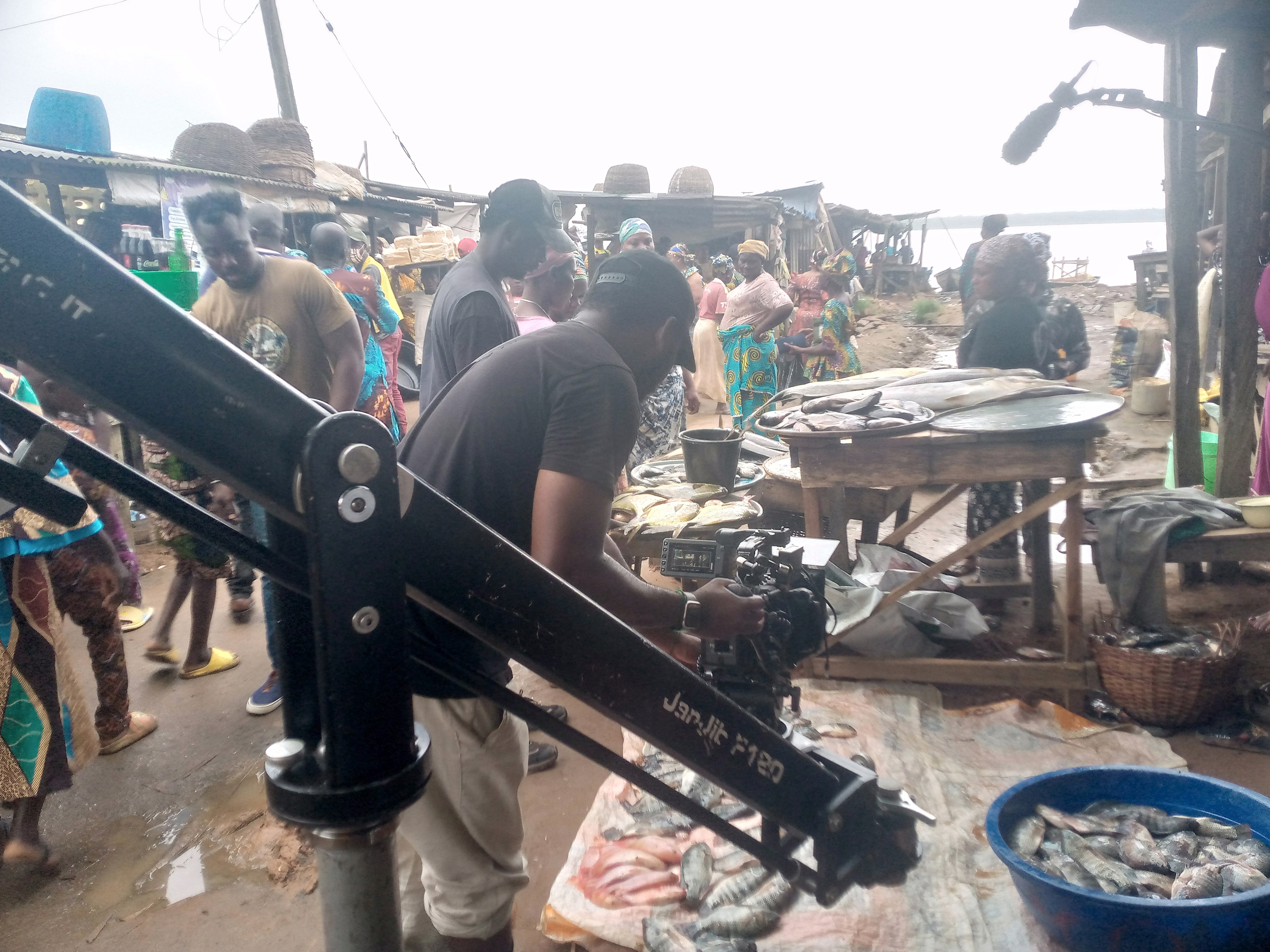 Camera operator on a jib crane filming at a busy riverside fish market